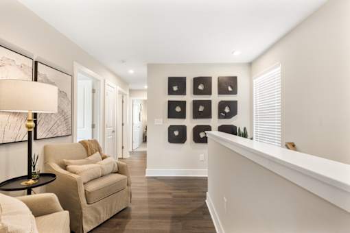 Open loft-style living area at Mural Lewis Center featuring wood-style flooring, neutral tones, accent wall art, cozy seating, and overlook railing for added space and light