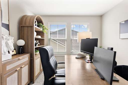 Modern home office at Mural Lewis Center featuring a large window with natural light, wood desk, computer setup, ergonomic chair, and built-in shelving for storage