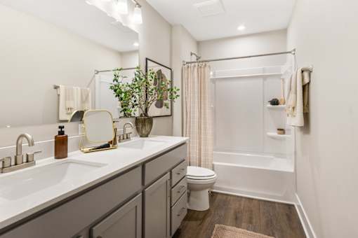 Contemporary apartment bathroom at Mural Lewis Center featuring double sink vanity, quartz countertops, large mirror, tub shower combination, and wood-style flooring