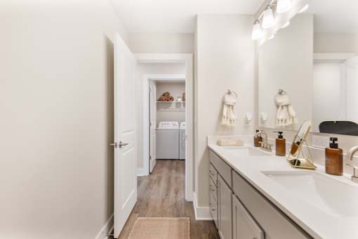 Spacious hallway bathroom in single-family rental home at Mural Lewis Center featuring double sink vanity, long countertop, large mirror, modern lighting, and wood-style flooring