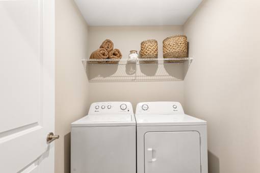 Laundry room in single-family rental home at Mural Lewis Center featuring full-size washer and dryer, overhead shelf storage, and clean, modern design