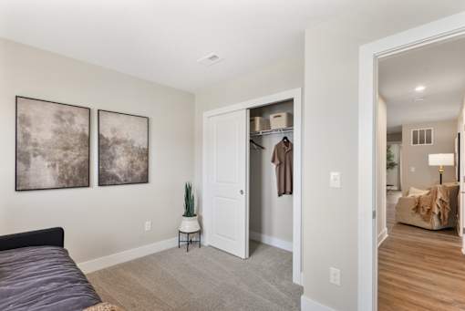 Bedroom in single-family rental home at Mural Lewis Center featuring plush carpeting, neutral walls, walk-in closet with sliding door, wall art, and view into spacious living area