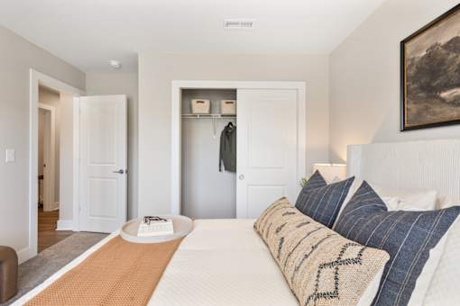 Clean and modern apartment bedroom at Mural Lewis Center featuring neutral tones, ceiling fan, walk-in closet access, soft carpeting, and contemporary decor