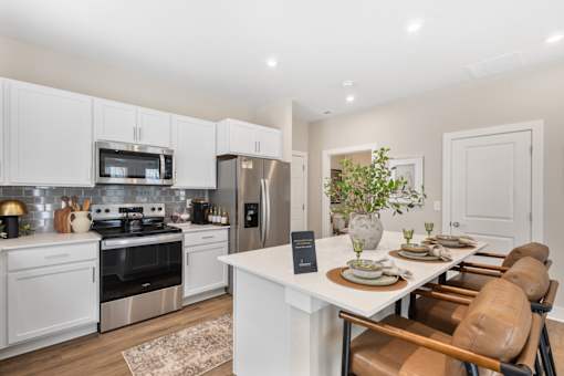 Open-concept apartment kitchen at Mural Lewis Center featuring large island with seating, white cabinetry, stainless steel appliances, subway tile backsplash, and wood-style flooring
