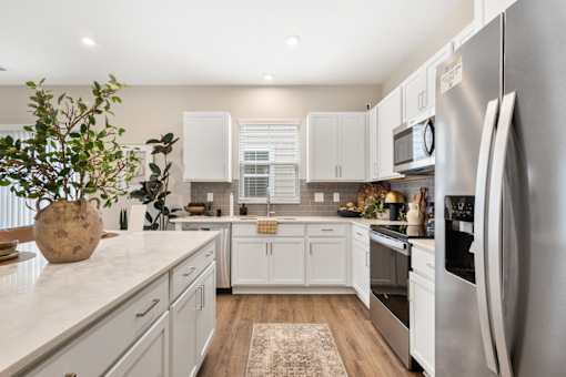 Bright modern apartment kitchen at Mural Lewis Center featuring white shaker cabinets, quartz countertops, stainless steel appliances, kitchen island, and wood-style flooring