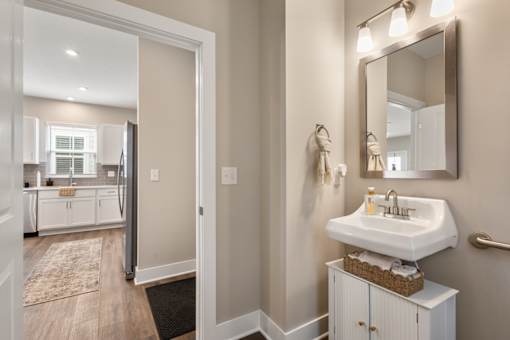Stylish guest bathroom at Mural Lewis Center featuring modern vanity, large mirror, updated lighting fixtures, neutral tones, and easy access from hallway