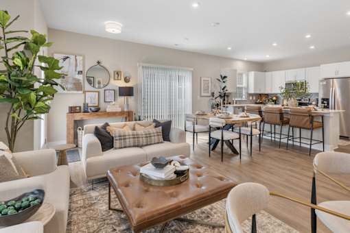 Open-concept living room in single-family rental home at Mural Lewis Center featuring wood-style flooring, neutral tones, modern furnishings, large windows, and seamless connection to dining area