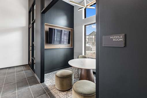 Modern huddle room at Nook Nine with a TV, cozy seating, and natural light for collaboration.