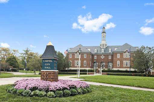 a large brick building with a sign in front of a lawn with flowers at Gramercy Apartments, Indiana, 46032