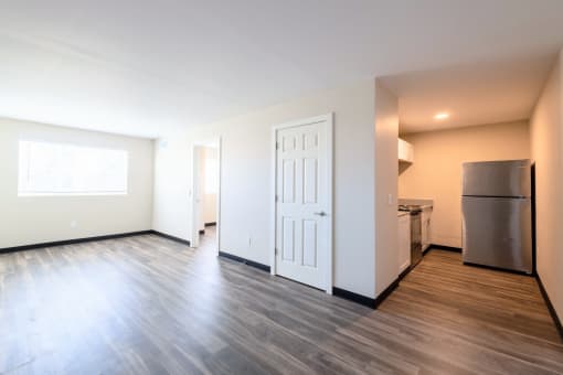 the living room and kitchen of an apartment with wood flooring and a refrigerator