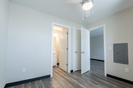 a living room with white walls and wood flooring and a door to a bathroom