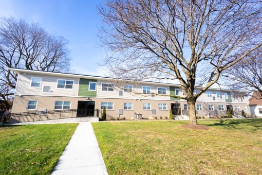 the exterior of an apartment building with a sidewalk and a tree