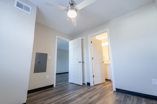 a living room with white walls and wood floors and a door to a bathroom