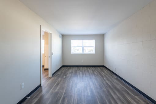 the living room of an empty apartment with wood flooring and a window
