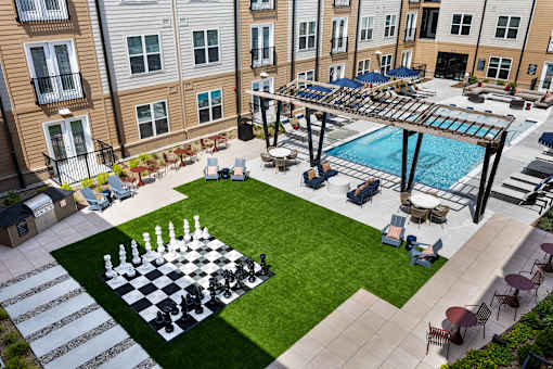 Oversized outdoor chess set placed on a grassy lawn next to the swimming pool at Portrait Midtown apartments.