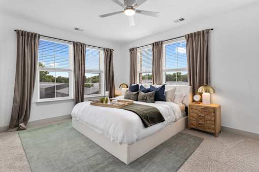 Spacious apartment bedroom featuring high ceilings with a modern ceiling fan, plush neutral carpeting, and expansive windows that fill the space with abundant natural light.