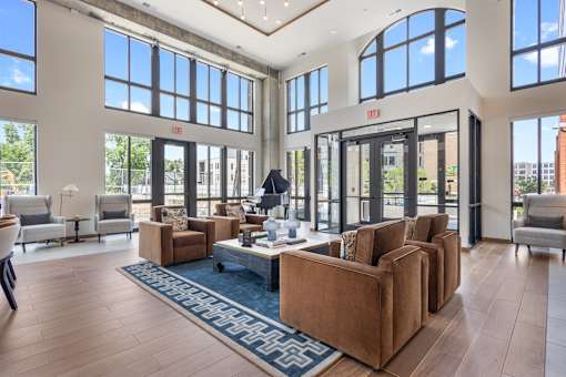 Soaring double-height leasing center featuring massive floor-to-ceiling windows, polished flooring, contemporary lighting fixtures, and a spacious layout with comfortable lounge seating.