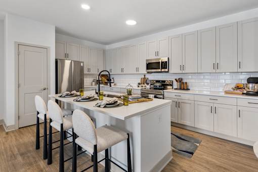 Kitchen with sleek light-wood cabinetry, white countertops, a stainless steel under-mount sink with a modern gooseneck faucet, and contemporary built-in appliances.