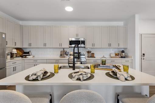 Modern apartment kitchen showcasing crisp white quartz countertops, contemporary light-wood cabinets, a spacious island, and high-end stainless steel appliances.