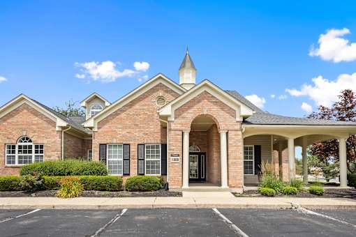 Welcoming leasing office with classic brick architecture, landscaped entrance, and covered porte cochère at Steeplechase at Shiloh Crossing Apartments in Avon, Indiana.