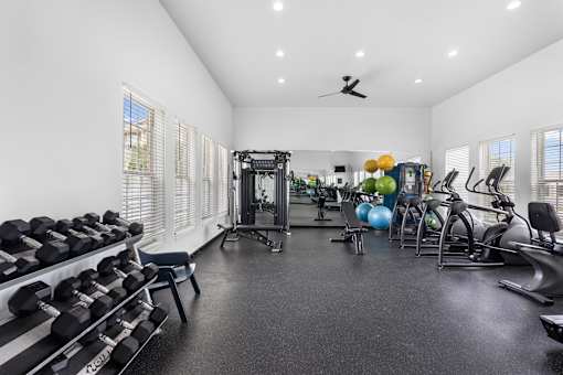 Spacious 24-hour fitness center featuring free weights, strength training equipment, cardio machines, mirrored walls, and natural light at Steeplechase at Shiloh Crossing Apartments in Avon, Indiana.