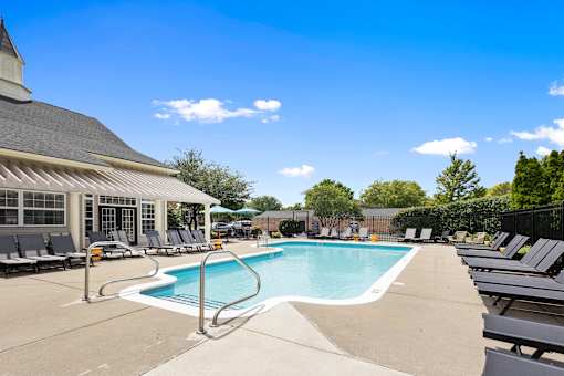 Resort-style outdoor swimming pool featuring a spacious sundeck, poolside lounge chairs, shaded seating, and beautifully landscaped grounds at Steeplechase at Shiloh Crossing Apartments in Avon, Indiana.