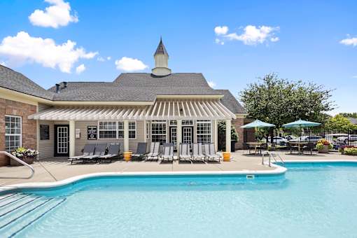 Resort-style outdoor swimming pool with poolside lounge chairs, shaded seating, and the resident clubhouse at Steeplechase at Shiloh Crossing Apartments in Avon, Indiana.