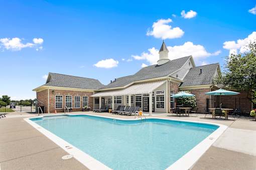Resort-style outdoor swimming pool with lounge seating, shaded patio areas, and the resident clubhouse at Steeplechase at Shiloh Crossing Apartments in Avon, Indiana.