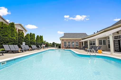 Resort-style outdoor swimming pool with spacious sundeck, lounge chairs, and the resident clubhouse at Steeplechase at Shiloh Crossing Apartments in Avon, Indiana.