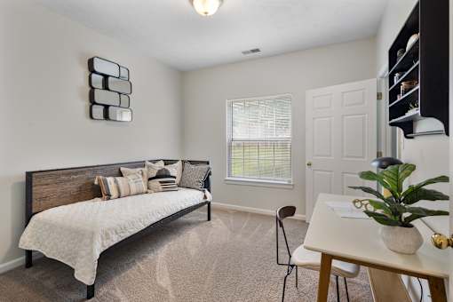 Versatile apartment flex space featuring a daybed, dedicated workspace, plush carpeting, and a large window with natural light at Steeplechase at Shiloh Crossing Apartments in Avon, Indiana.