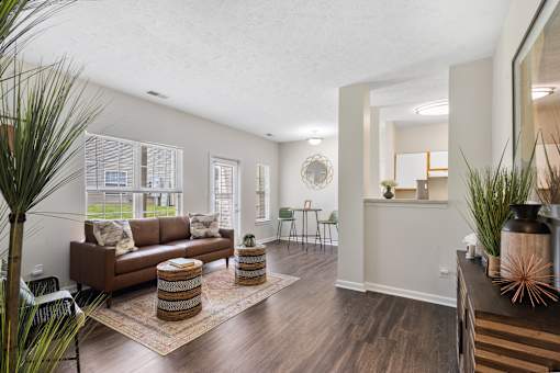 Bright open-concept apartment featuring a spacious living room, wood-style flooring, breakfast bar, and dining area at Steeplechase at Shiloh Crossing Apartments in Avon, Indiana.