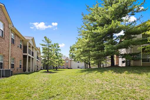 Beautifully landscaped community grounds featuring mature trees, open green space, and apartment homes with private balconies at Steeplechase at Shiloh Crossing Apartments in Avon, Indiana.