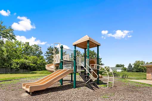 Children's playground with slides and climbing features surrounded by landscaped green space at Steeplechase at Shiloh Crossing Apartments in Avon, Indiana.