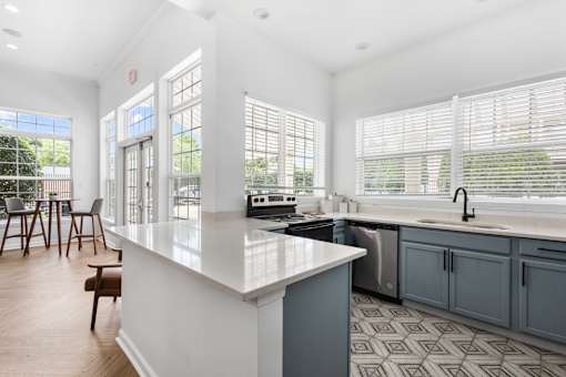 Modern resident clubhouse kitchen featuring quartz countertops, updated cabinetry, stainless steel appliances, and large windows overlooking the community at Steeplechase at Shiloh Crossing Apartments in Avon, Indiana.