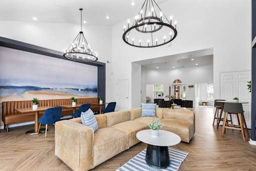 Spacious resident clubhouse with comfortable lounge seating, coworking tables, vaulted ceilings, designer lighting, and modern finishes at Steeplechase at Shiloh Crossing Apartments in Avon, Indiana.