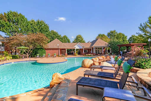 Resort-style swimming pool with lounge chairs, lush landscaping, and clubhouse at Village at Almand Creek apartments in Conyers, GA. Perfect for relaxation and outdoor living.