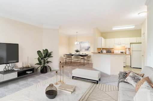 Spacious open-concept living room, dining area, and kitchen in an upscale apartment at Village at Almand Creek in Conyers, GA. Features modern furnishings, natural light, and elegant design.