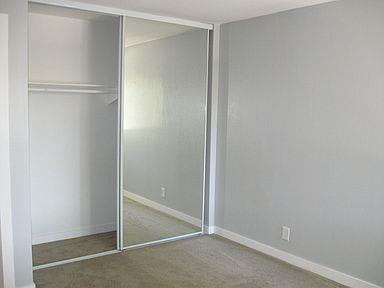 An empty bedroom with tan carpets and a sliding mirror doors to the closet