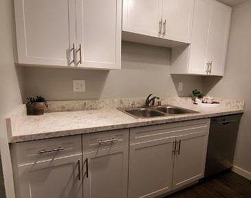 A kitchen with all white cabinets and chrome handles. The sink is in the middle.