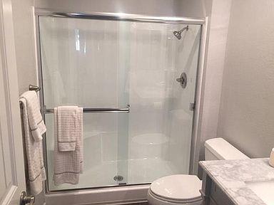 The bathroom with a tub & shower combo that has glass doors. A towel lays on the bar of the door. The toilet is in middle and a sink barely visible on the right