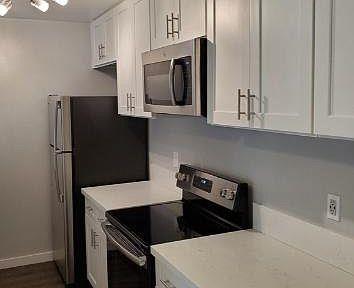 A kitchen with stainless steel appliances including a microwave, an oven and stove, and fridge. The cabinets are all white with chrome handles.