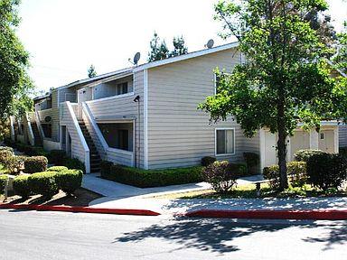  A picture taken from across the street of building 7 with a tree on the right side, a sidewalk in the middle, and bushes on the left.