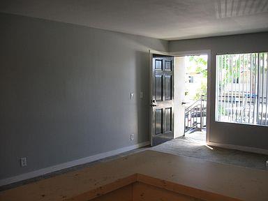 An empty living room looks out on an open front door with trees outside.