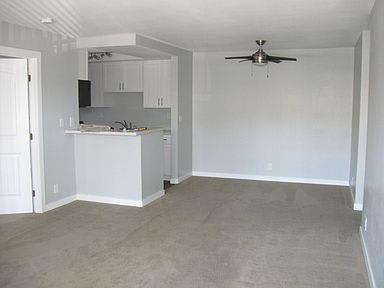 Large empty living room with an open-concept kitchen. A chrome fan is in the middle.