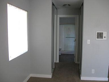 A large empty bedroom looks down the hallway lined with closets to the entryway into the bathroom
