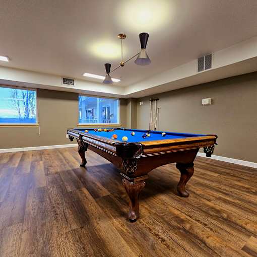 A pool table in a room with wooden flooring and a light fixture.