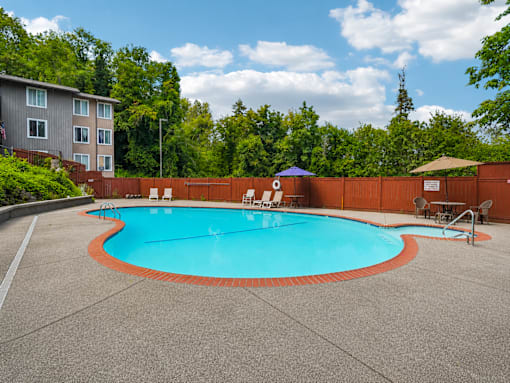 A small pool with a blue umbrella and a brown fence.