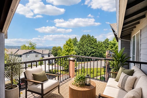 A balcony with a chair, couch, and table with a view of the neighborhood.