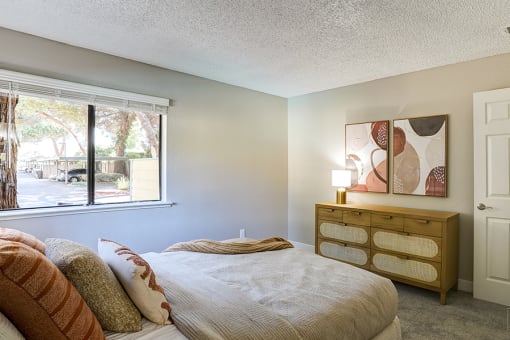 One-Bedroom Apartments in Hayward, CA - Austin Commons - Bedroom with Modern Bedspread, Wooden Dresser, and Large Window