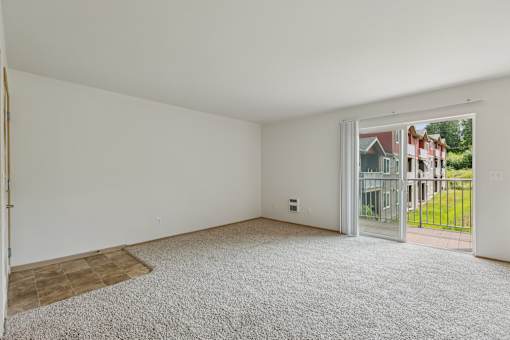 A room with white walls and a carpeted floor with a doorway leading to a balcony.